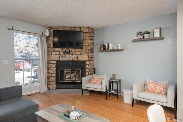 living area featuring visible vents, a textured ceiling, wood finished floors, a fireplace, and baseboards