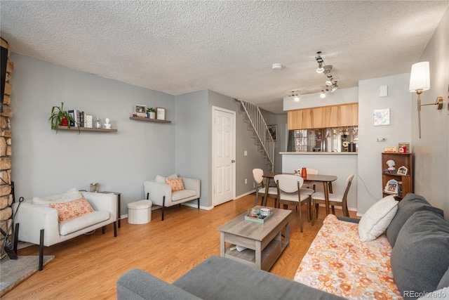 living area with a textured ceiling, rail lighting, light wood finished floors, baseboards, and stairs