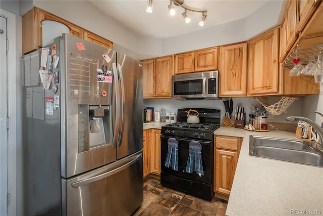 kitchen with a sink, stone finish flooring, appliances with stainless steel finishes, and light countertops