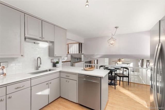 kitchen featuring pendant lighting, appliances with stainless steel finishes, sink, kitchen peninsula, and gray cabinetry