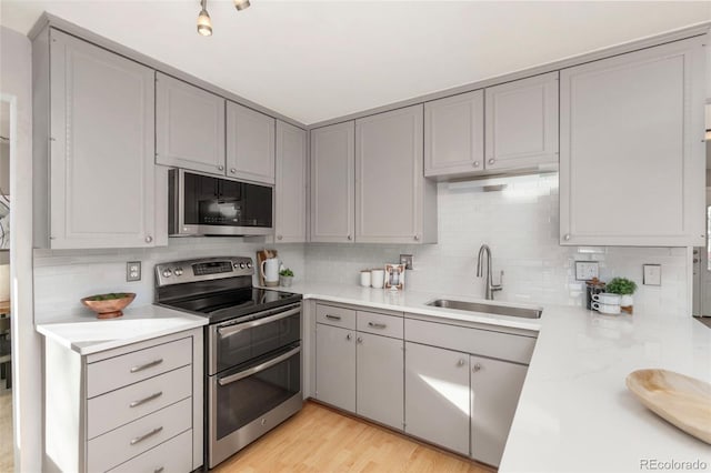 kitchen featuring decorative backsplash, gray cabinets, light countertops, double oven range, and a sink