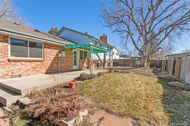 rear view of house featuring a patio, brick siding, a lawn, and a fenced backyard