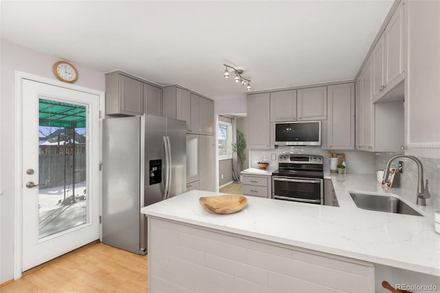 kitchen with gray cabinetry, appliances with stainless steel finishes, a sink, light stone countertops, and a peninsula