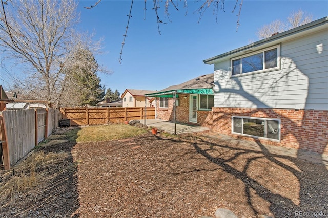 rear view of house featuring brick siding, a fenced backyard, and a patio