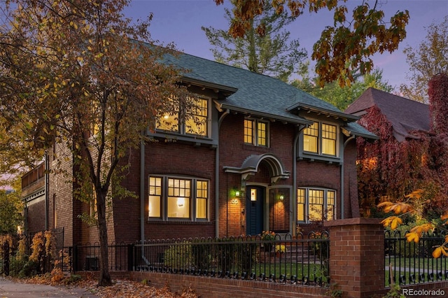 view of front facade featuring roof with shingles, brick siding, and a fenced front yard