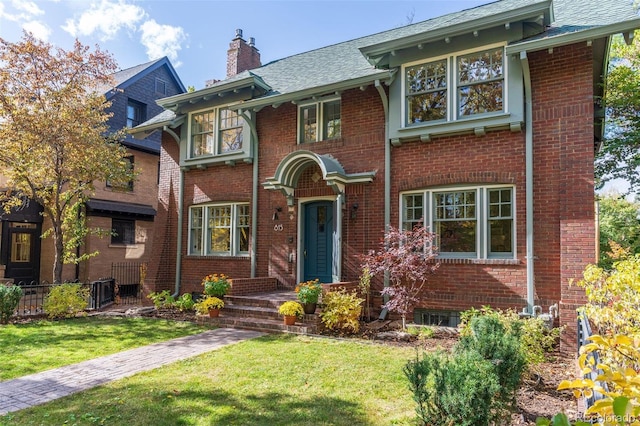 view of front facade featuring brick siding, a chimney, and a front lawn