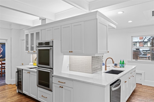 kitchen featuring stainless steel double oven, beverage cooler, a sink, light wood-style floors, and decorative backsplash