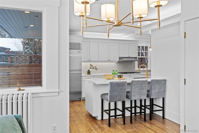 kitchen with light wood-style floors, radiator, stainless steel built in fridge, and under cabinet range hood