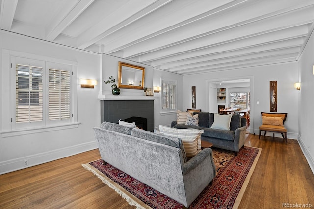 living room with a warm lit fireplace, wood finished floors, beam ceiling, and baseboards