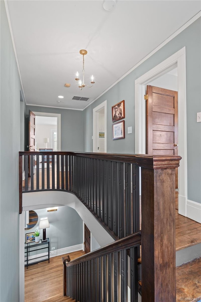 stairway featuring wood finished floors, visible vents, baseboards, ornamental molding, and an inviting chandelier