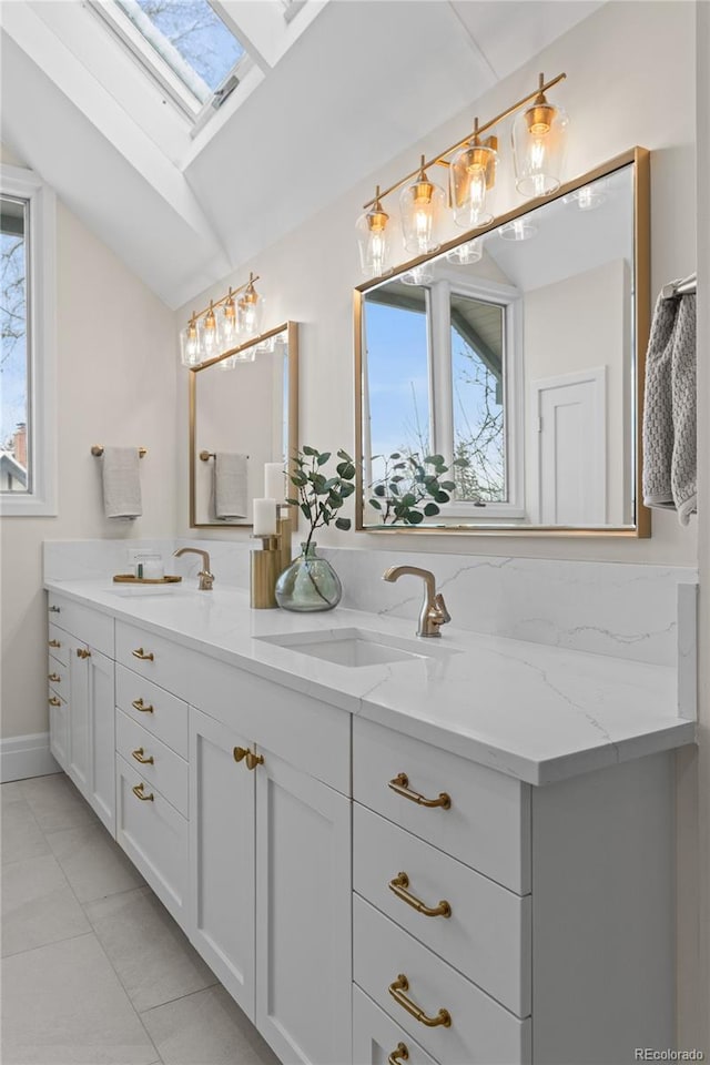 full bath with double vanity, lofted ceiling with skylight, a sink, and tile patterned floors