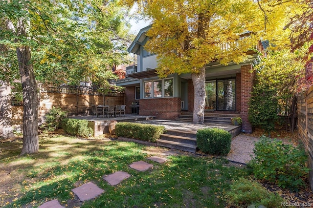 view of front of home with brick siding, fence, a balcony, and a front lawn