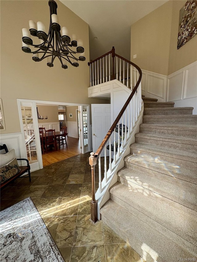 staircase with wainscoting, a decorative wall, a chandelier, stone finish floor, and a towering ceiling