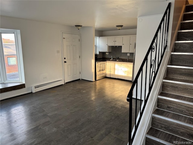 kitchen featuring dark wood finished floors, tasteful backsplash, dark countertops, baseboard heating, and stainless steel range oven