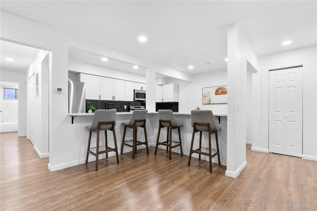 kitchen with white cabinetry, stainless steel appliances, kitchen peninsula, a kitchen bar, and light wood-type flooring