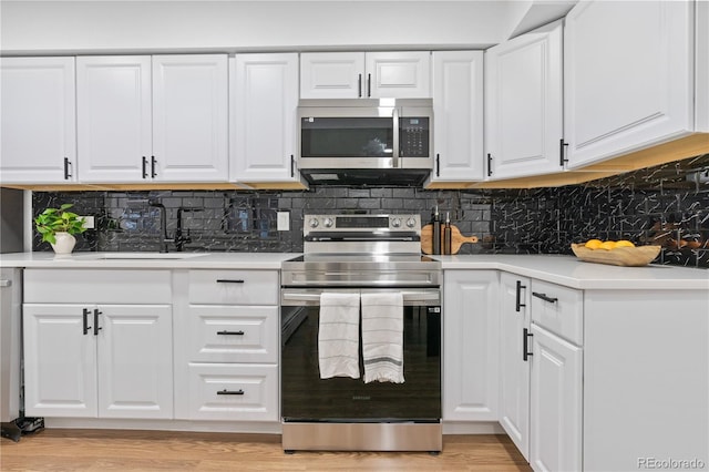 kitchen featuring light wood-type flooring, backsplash, stainless steel appliances, sink, and white cabinets