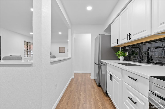 kitchen with backsplash, sink, light hardwood / wood-style flooring, dishwasher, and white cabinetry