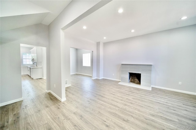 unfurnished living room with sink, light hardwood / wood-style flooring, vaulted ceiling, and a premium fireplace