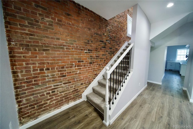 stairs with hardwood / wood-style floors and brick wall