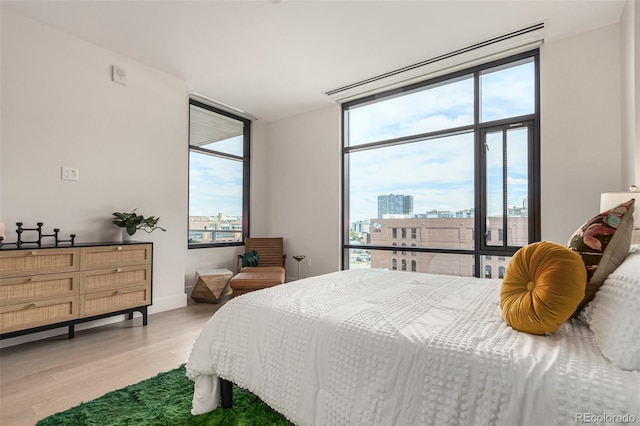 bedroom featuring baseboards, multiple windows, light wood-style flooring, and a city view