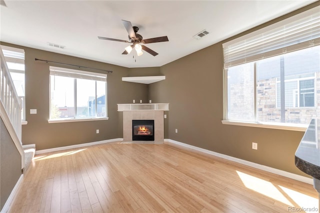 unfurnished living room with visible vents, hardwood / wood-style floors, ceiling fan, stairway, and a tiled fireplace