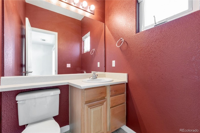 bathroom featuring vanity, a textured wall, visible vents, and toilet
