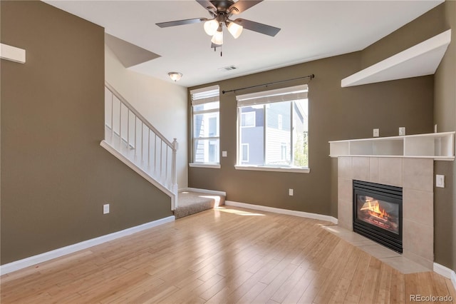 unfurnished living room with stairs, visible vents, light wood finished floors, and a tile fireplace