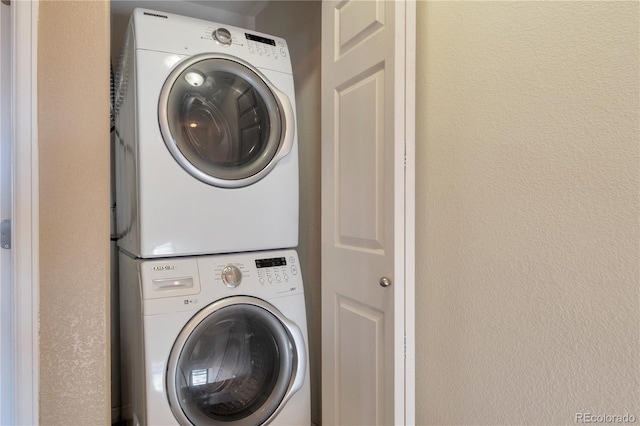 washroom with a textured wall, laundry area, and stacked washer and dryer