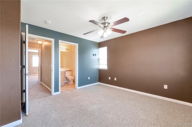 unfurnished bedroom with light colored carpet, baseboards, ensuite bath, and multiple windows