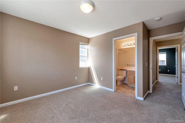 unfurnished bedroom with connected bathroom, baseboards, and light colored carpet