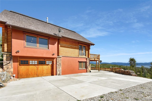 back of house with stucco siding, a shingled roof, a mountain view, a balcony, and log siding