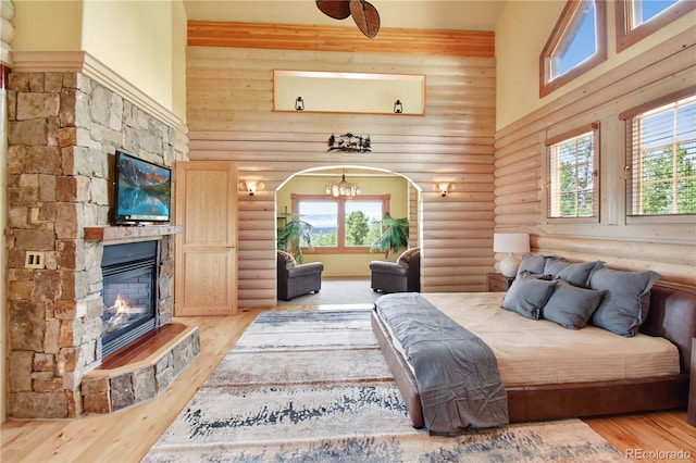 bedroom with rustic walls, a fireplace, a towering ceiling, and light wood finished floors