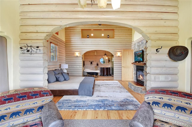 living room featuring rustic walls, hardwood / wood-style floors, a towering ceiling, and a stone fireplace