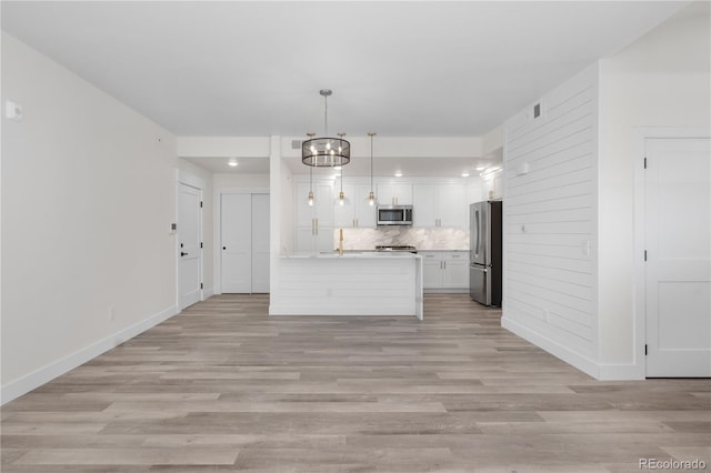 kitchen with appliances with stainless steel finishes, tasteful backsplash, light hardwood / wood-style floors, white cabinets, and decorative light fixtures