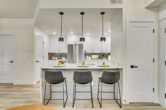 kitchen featuring light countertops, hanging light fixtures, freestanding refrigerator, white cabinetry, and a peninsula