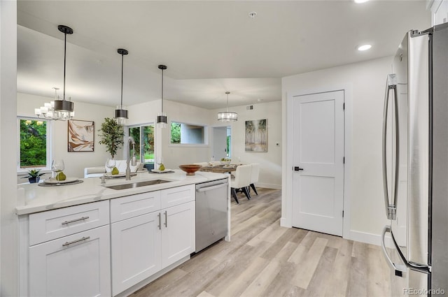 kitchen with decorative light fixtures, a notable chandelier, stainless steel appliances, white cabinets, and a sink