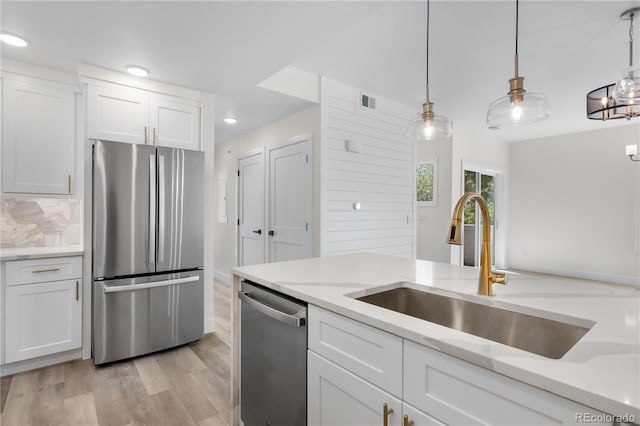 kitchen featuring light stone counters, hanging light fixtures, appliances with stainless steel finishes, white cabinetry, and a sink