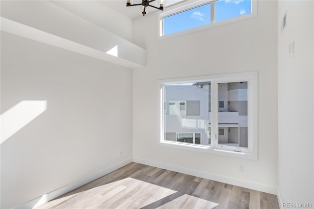 empty room featuring light wood-style floors, a high ceiling, baseboards, and an inviting chandelier