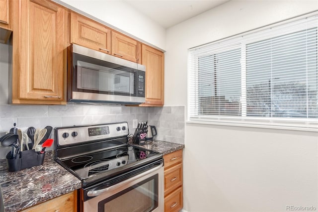 kitchen featuring stainless steel appliances, dark stone counters, and backsplash