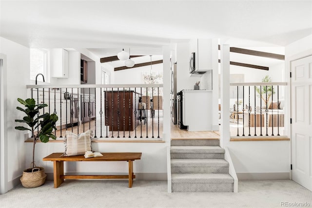 staircase featuring an inviting chandelier, lofted ceiling with beams, and carpet flooring