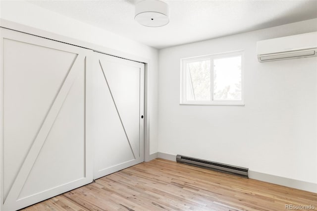 unfurnished bedroom featuring baseboard heating, a closet, a wall mounted AC, and light wood-type flooring