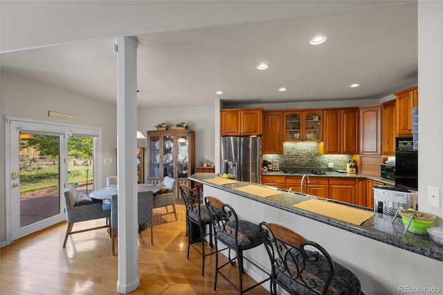 332 Battlement Creek Trl, Parachute, CO 81635 - kitchen with stainless steel fridge, brown cabinets, a peninsula, glass insert cabinets, and decorative backsplash