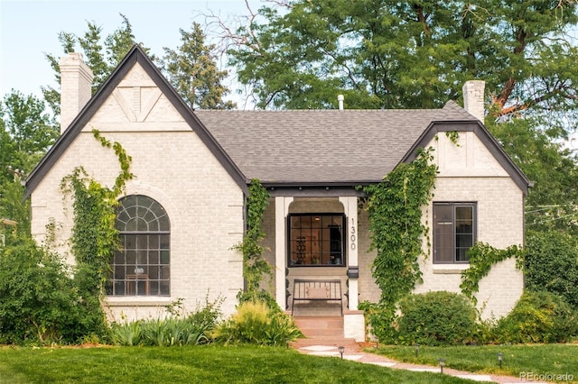 1300 N Glencoe St, Denver, CO 80220 - english style home featuring a chimney, brick siding, roof with shingles, and a front yard