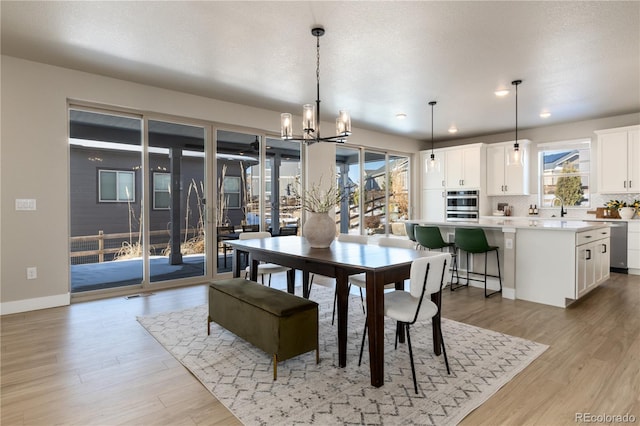 dining area featuring an inviting chandelier, a healthy amount of sunlight, sink, and light wood-type flooring