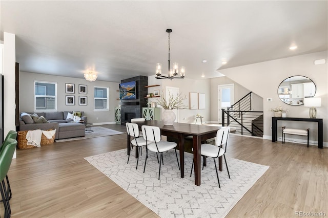 dining space featuring a notable chandelier, a fireplace, and light wood-type flooring