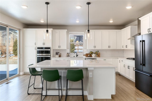 kitchen with a center island, black refrigerator, pendant lighting, and white cabinets