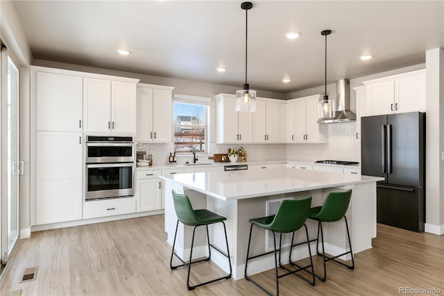 kitchen featuring wall chimney range hood, a center island, light hardwood / wood-style floors, black appliances, and white cabinets