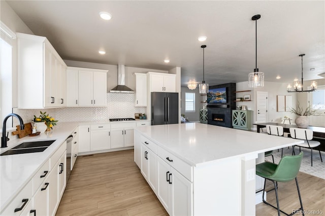 kitchen featuring pendant lighting, sink, black appliances, a kitchen island, and wall chimney exhaust hood