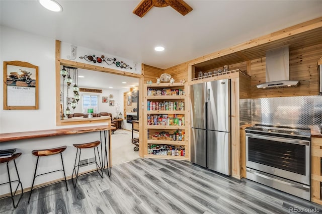 kitchen with a breakfast bar area, decorative backsplash, hardwood / wood-style flooring, stainless steel appliances, and wall chimney exhaust hood