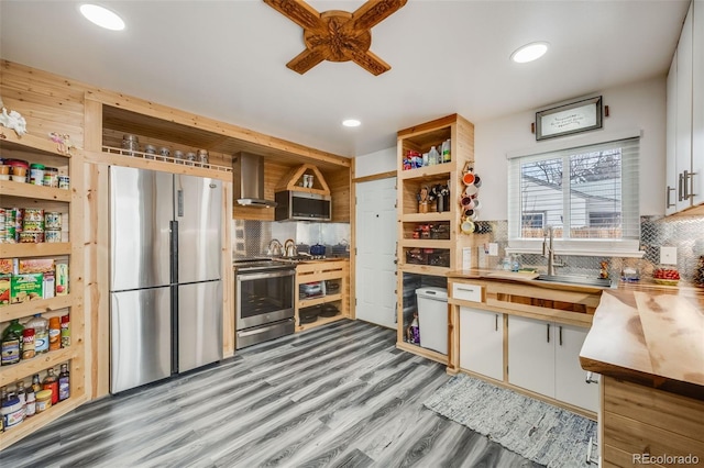 kitchen with wall chimney exhaust hood, white cabinetry, wooden counters, appliances with stainless steel finishes, and decorative backsplash